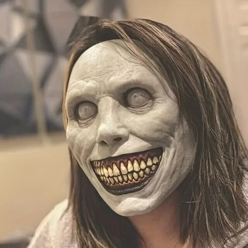 A woman is wearing a realistic smiling demon latex mask with exaggerated teeth and facial features.