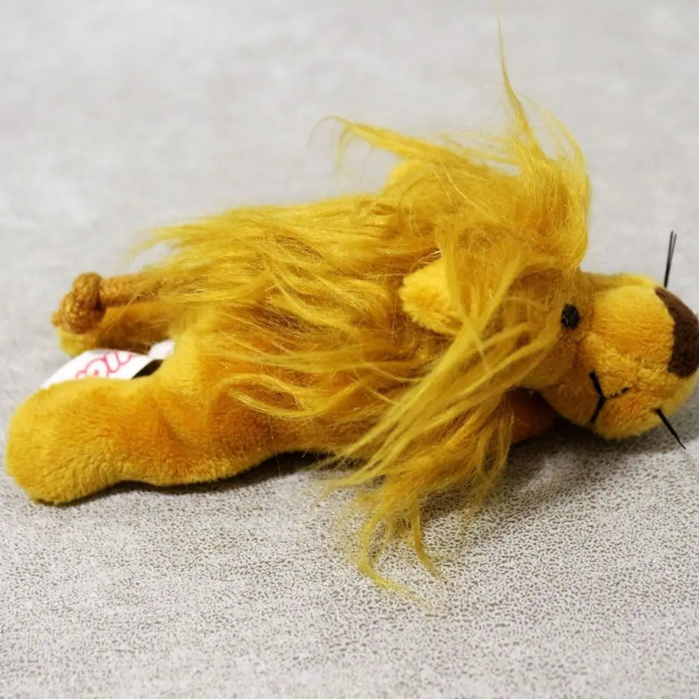 A fluffy yellow lion plush toy lying on a gray textured surface.