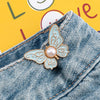 A delicate light blue enamel butterfly clip with a pearl accent is shown attached to denim fabric.