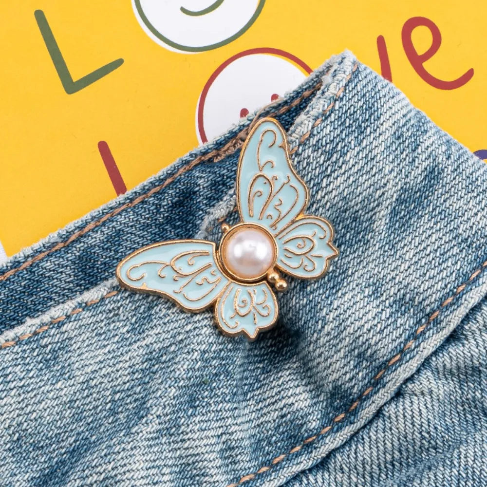A delicate light blue enamel butterfly clip with a pearl accent is shown attached to denim fabric.