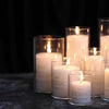 A collection of clear glass candle holders with white candles arranged on a dark surface.