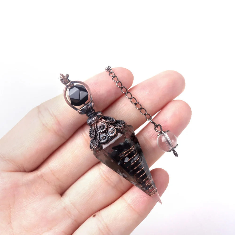 A hand holds a natural crystal pendulum necklace set featuring a dark, pointed crystal pendant on a chain.