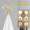 A gold brass bowknot wall hook is shown hanging on a white fabric, demonstrating its ability to be applied to multiple items.