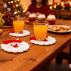 A set of handmade crochet Santa Claus coasters with orange juice glasses on a wooden table.