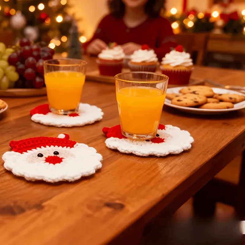 A set of handmade crochet Santa Claus coasters with orange juice glasses on a wooden table.