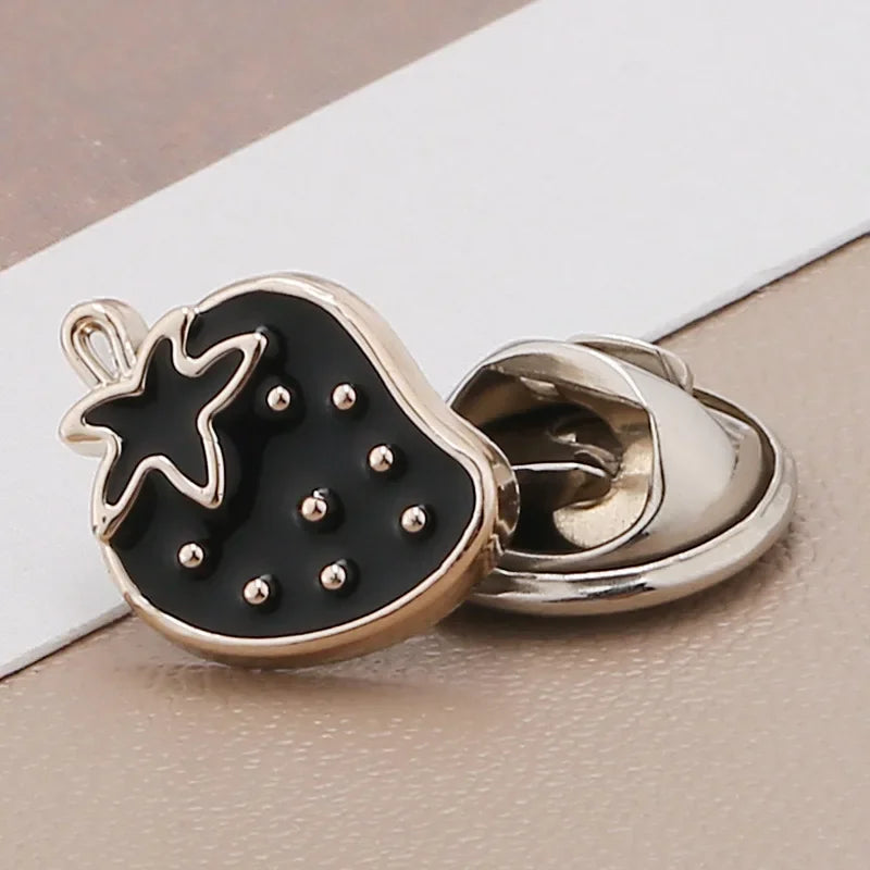 A black fruit-shaped brooch button with a silver finding, featuring a star design and small rhinestones.