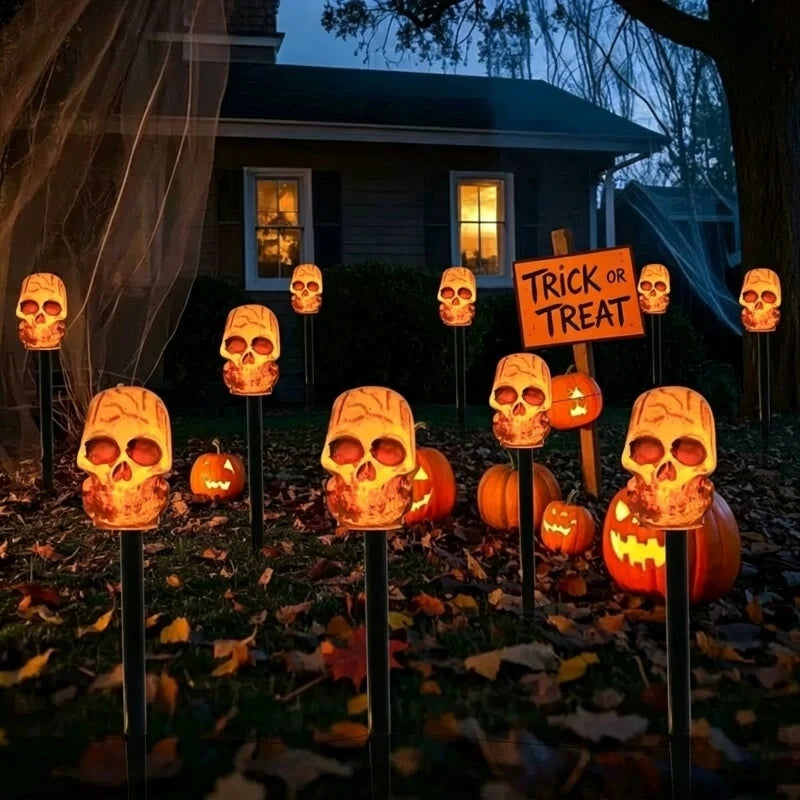 A row of glowing skull lanterns on stakes in a garden setting for Halloween decorations.
