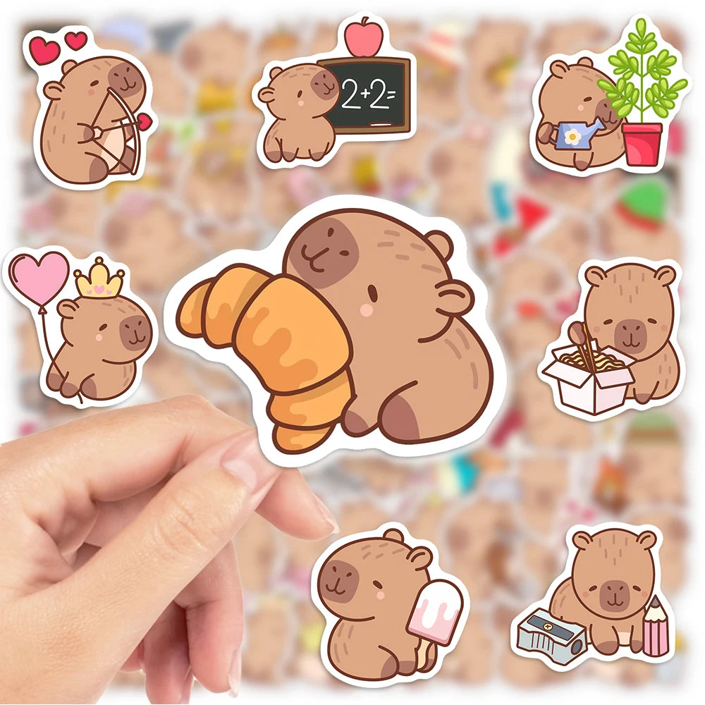 Hand holding a cute brown bear decal sticker on a finger against a background of various stickers.
