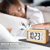 A hand is pressing the snooze button on a wooden digital alarm clock used for daily alarms with snoozing.