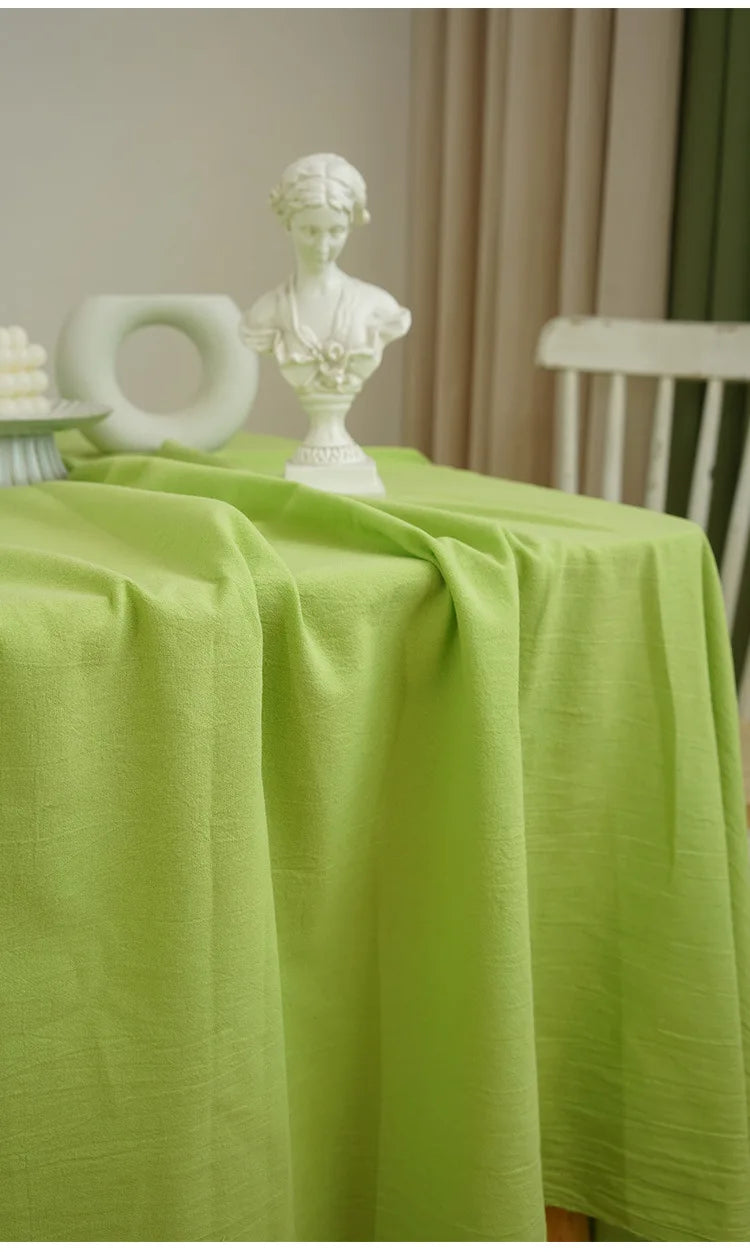 A lime green classic cotton rectangle tablecloth draped on a table with a white sculpted figure.