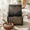 An antique wood music box with an engraved melody sits in a wooden box on a linen cloth.