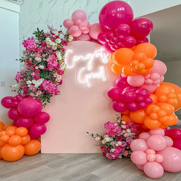 A balloon garland featuring pink and orange balloons arranged on a light pink backdrop.