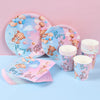 A set of pink and blue gender reveal party tableware including plates, cups, and a folded tablecloth with cute animal designs