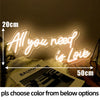 A glowing neon sign shaped like All you need is Love is displayed on a textured surface.