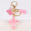 Gold-toned Christian cross charm with a pink resin butterfly and pink tassel on a keychain.