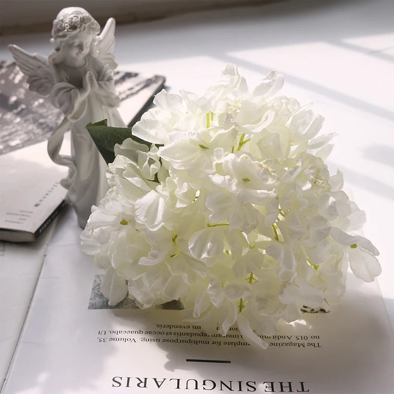 A bouquet of white silk hydrangea stems with vintage burnt edge petals displayed on a white surface.