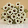 A cluster of three white silk gerbera daisy artificial flowers with dark centers on green foliage.