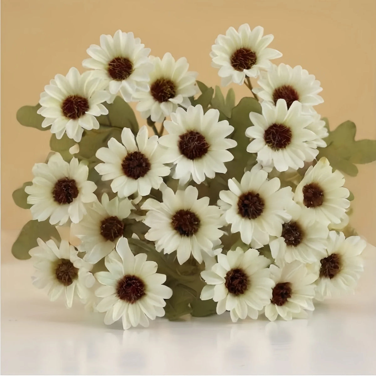 A cluster of three white silk gerbera daisy artificial flowers with dark centers on green foliage.