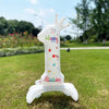 A white standing foil balloon shaped like a unicorn with a crown and birthday decorations on a green lawn.