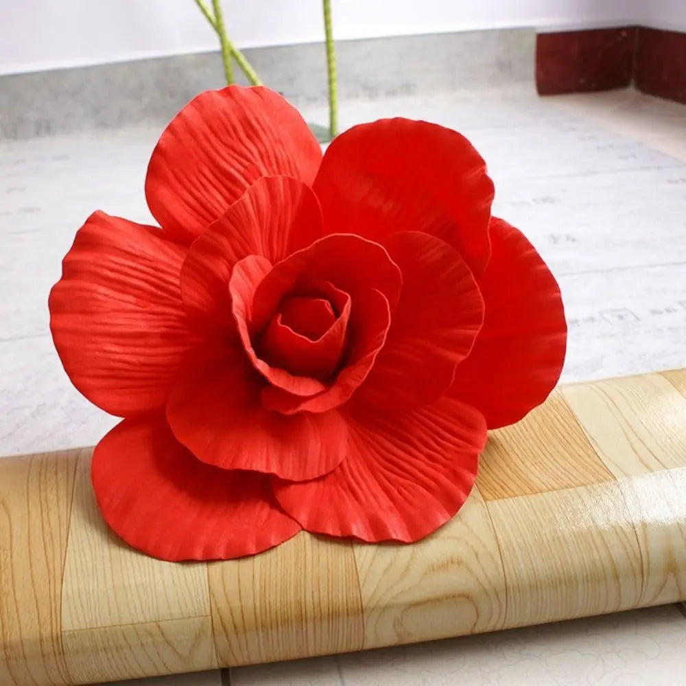 A vibrant red silk foam rose with green stem displayed on a wooden surface.