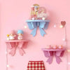 A pink wall shelf featuring decorative bow-shaped wooden shelves and a small figurine.