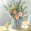 A bouquet of pink and peach roses and silvery-green eucalyptus stems in a woven basket for home decor.