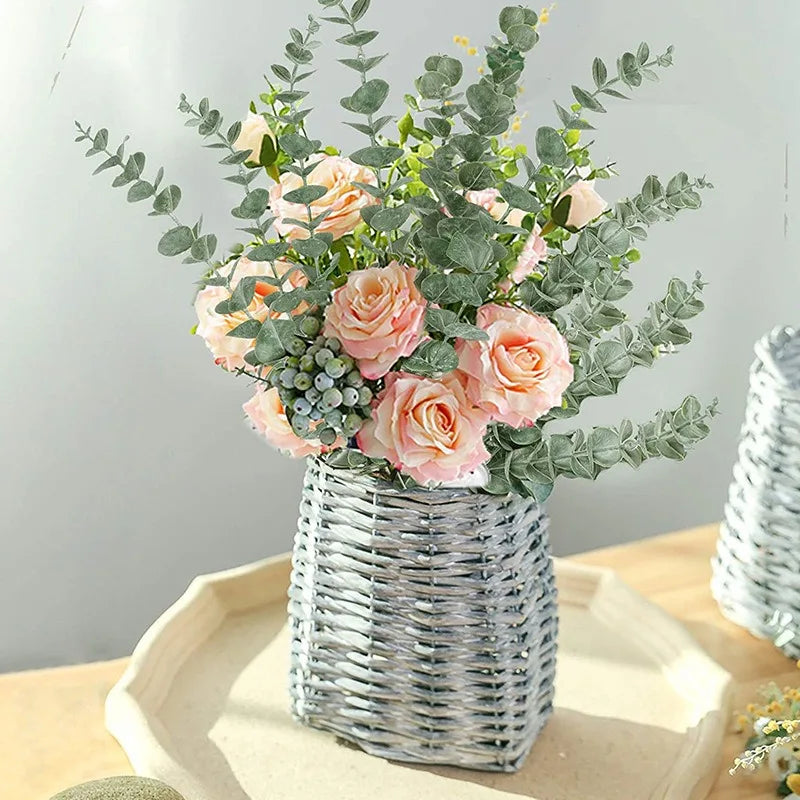 A bouquet of pink and peach roses and silvery-green eucalyptus stems in a woven basket for home decor.