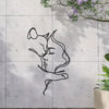 A black silhouette of a cat and a woman embracing is etched into a gray concrete wall with greenery above.