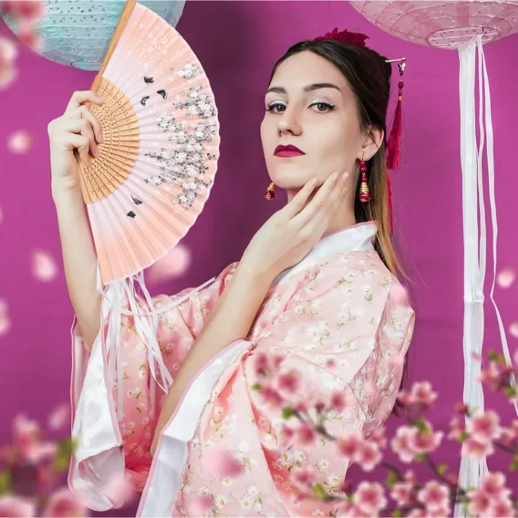 A woman in a pink floral kimono holds an orange bamboo folding hand fan against a purple background.