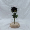 A preserved black rose with green leaves is displayed inside a glass dome on a wooden base.