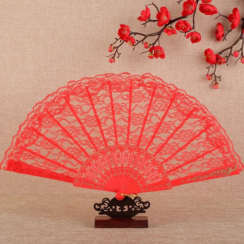 Red lace folding fan with black and white design displayed against a beige background with red flowers
