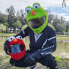 A person wearing a green cartoon plush helmet cover for a full-face motorcycle helmet outdoors.