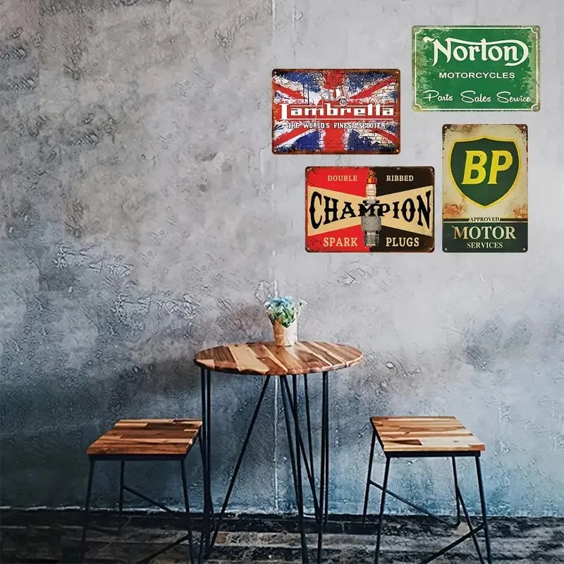 A collection of vintage metal tin signs featuring motorcycle and automotive themes displayed on a gray textured wall.