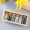 A wooden tray holds several small glass bottles with cork stoppers filled with various colored crystals and stones.