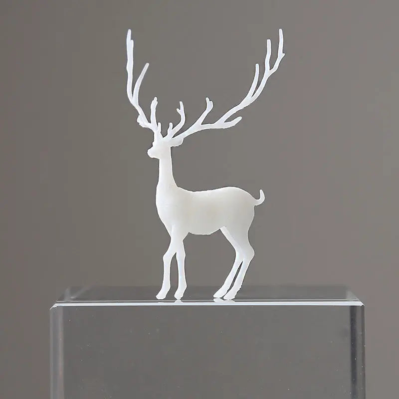 A white resin ornament of an elk deer with antlers standing on a clear glass base.