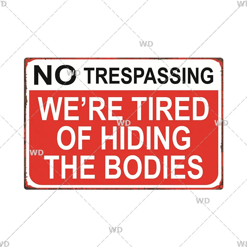 A vintage red metal warning sign with white text that reads NO TRESPASSING WE'RE TIRED OF HIDING THE BODIES