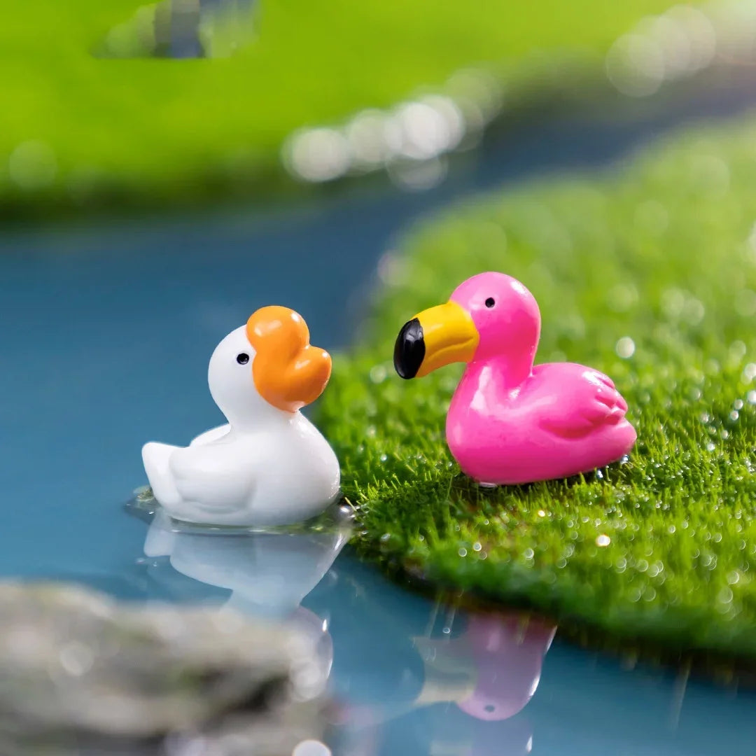 Deux petites sculptures animales en résine, un canard blanc et un flamant rose, reposant sur de la mousse verte dans de l'eau