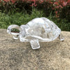 A clear crystal turtle desk ornament resting on a gray stone surface.