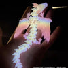 A hand holds a translucent, pink and white 3D printed articulated dragon fidget figurine with delicate wings.