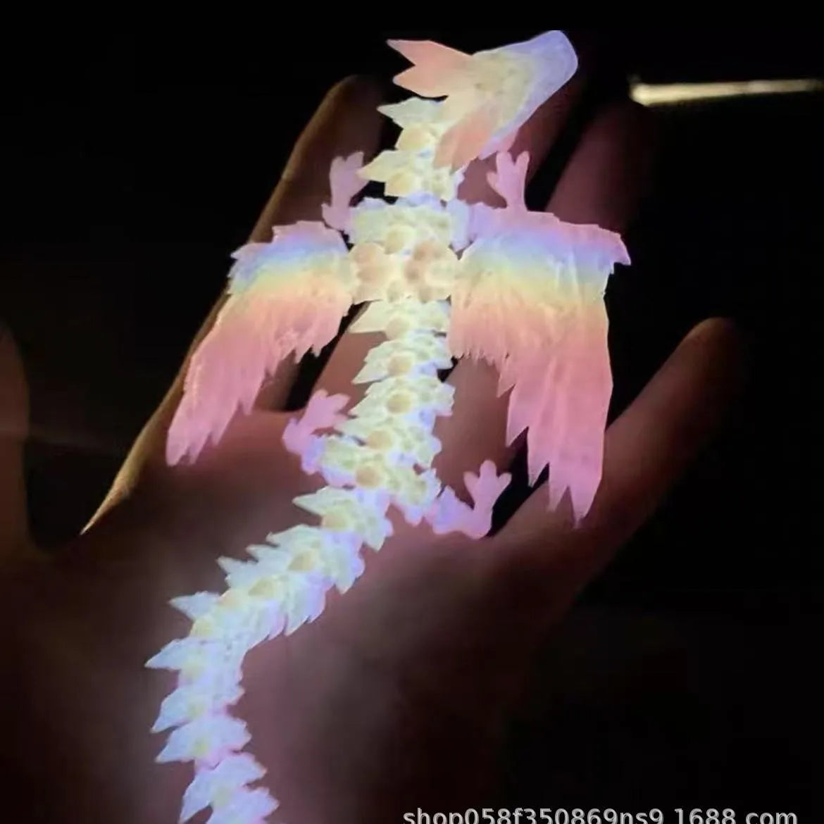 A hand holds a translucent, pink and white 3D printed articulated dragon fidget figurine with delicate wings.