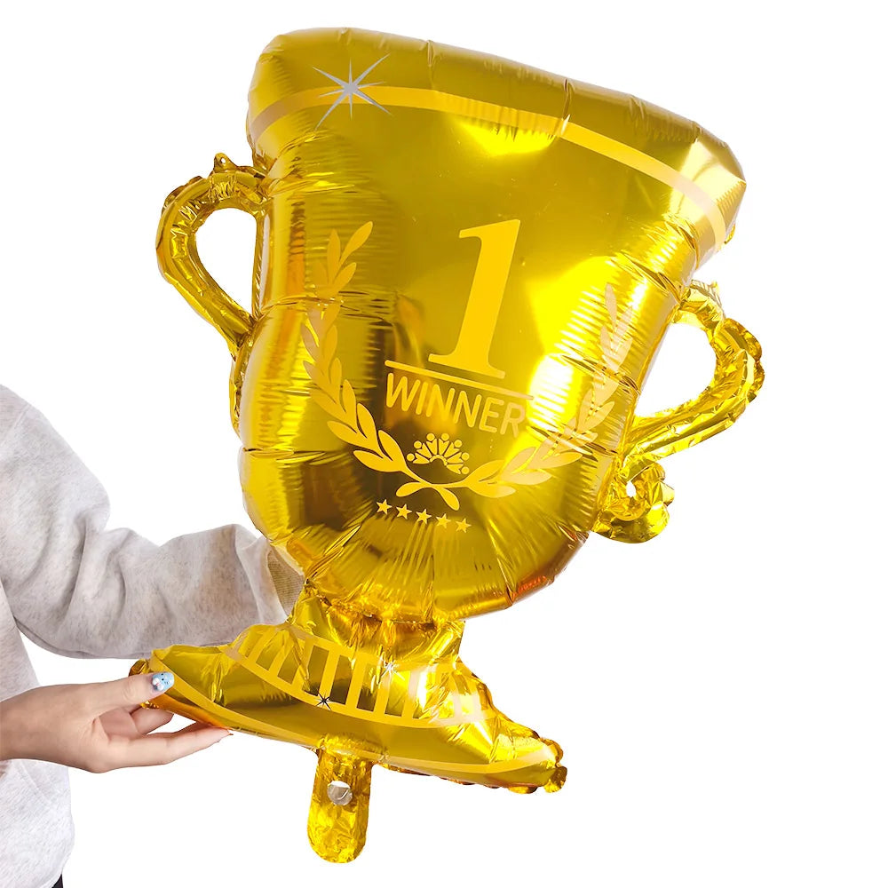 A golden foil soccer trophy balloon with the number 1 and winner text being held by a hand.