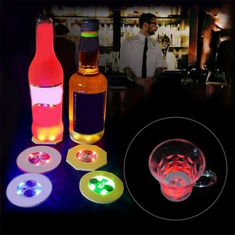 Luminous LED coaster lights illuminating bottles and glasses on a dark surface.