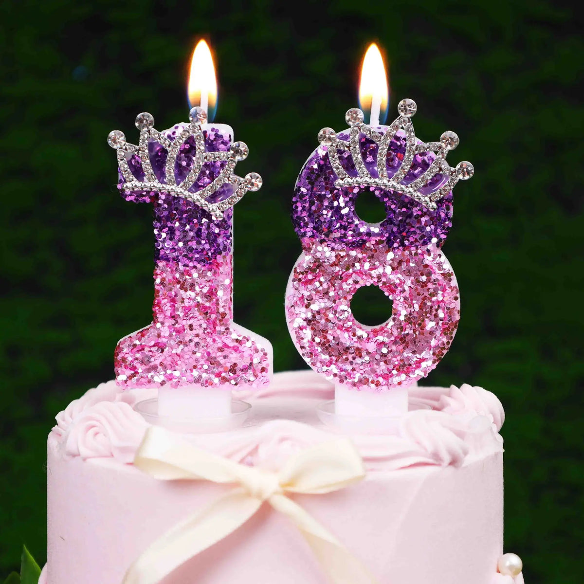 A pink cake decorated with a glitter number 18 candle and a rhinestone crown cake topper.