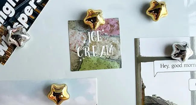 A collection of gold star-shaped fridge magnets and a sign reading ICE CREAM on a white surface.