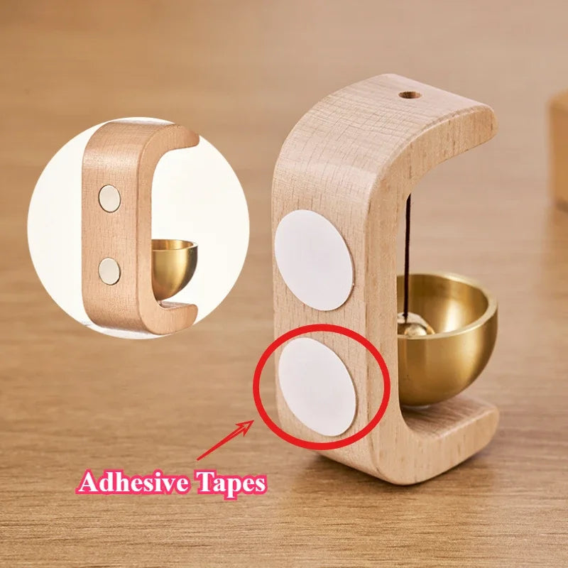 A wooden doorbell featuring a copper bell and adhesive tapes, shown in a close-up view.