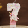 Vela de cumpleaños blanca con forma de 7 decorada con purpurina rosa y una pequeña figura de unicornio.