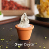 A clear green crystal is displayed in an orange terracotta pot on a dark surface.