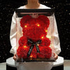 A red artificial rose teddy bear with a crown is displayed in a clear box for romantic gifts.
