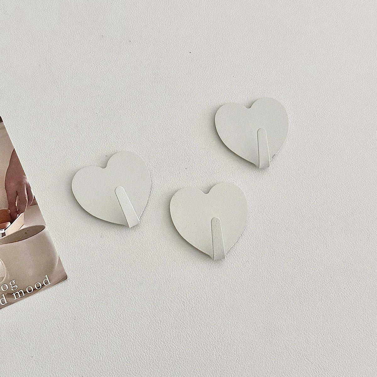 A set of three white heart-shaped adhesive key hooks for use in various rooms.