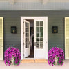 A white door with glass panels is framed by purple faux bougainvillea flowers on the ground.